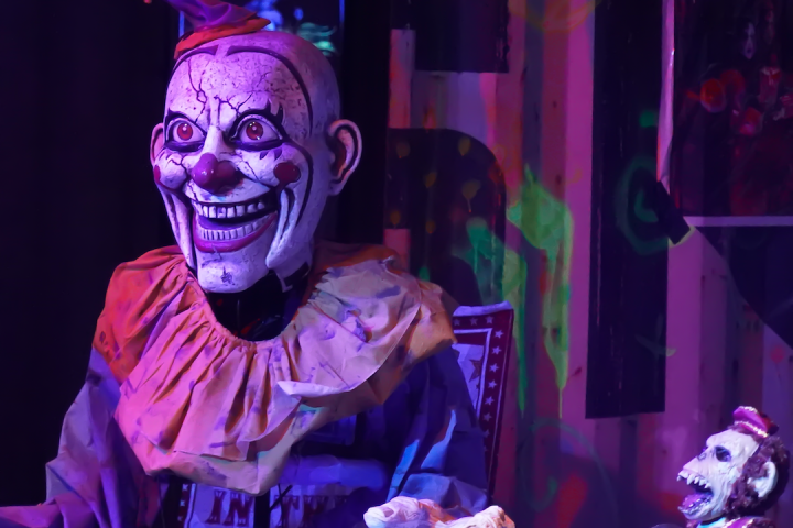 Creepy clown figure with a sinister grin in colorful lighting.