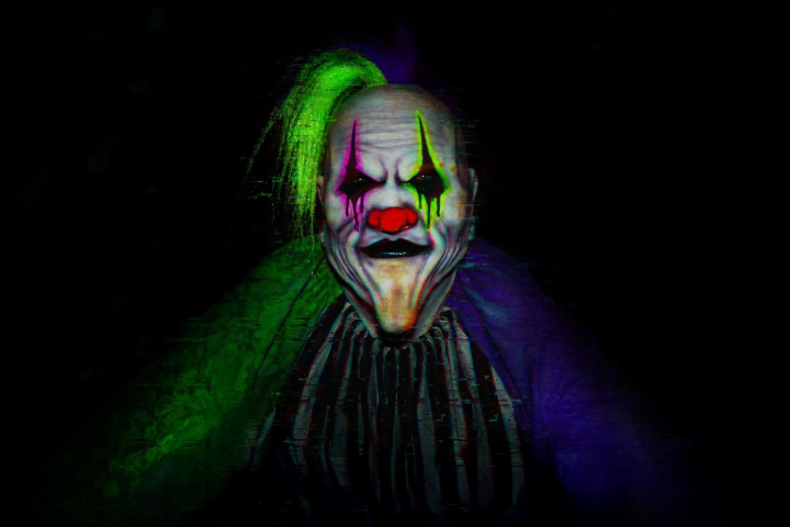 Creepy clown with green hair and striped outfit in dark setting.