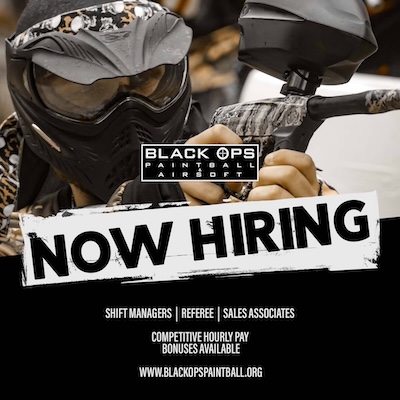 Person in paintball gear holding marker, 'Now Hiring' sign for Black Ops Paintball.